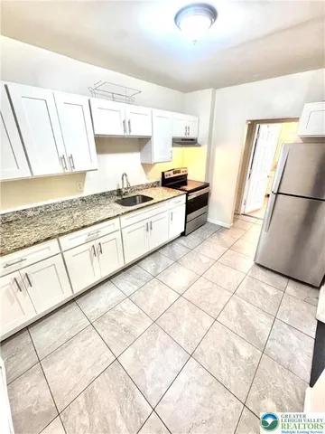 a large kitchen with a stove a sink dishwasher and white cabinets with wooden floor