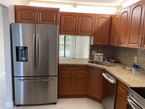 a kitchen with stainless steel appliances granite countertop a refrigerator a sink and white cabinets