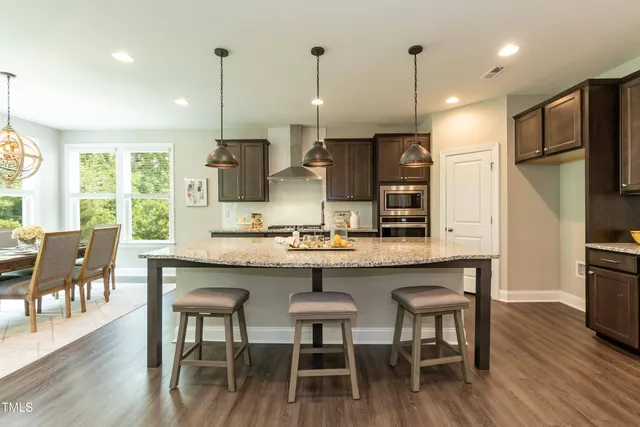 a kitchen with stainless steel appliances granite countertop a kitchen island a stove a refrigerator a kitchen island a dining table and chairs with wooden floor