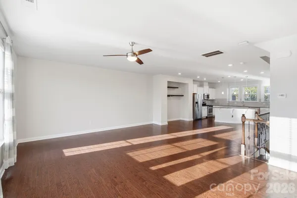 an empty room with wooden floor ceiling fan and windows