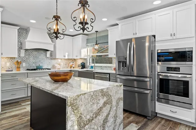 a kitchen with stainless steel appliances granite countertop a sink a stove a refrigerator cabinets and chairs