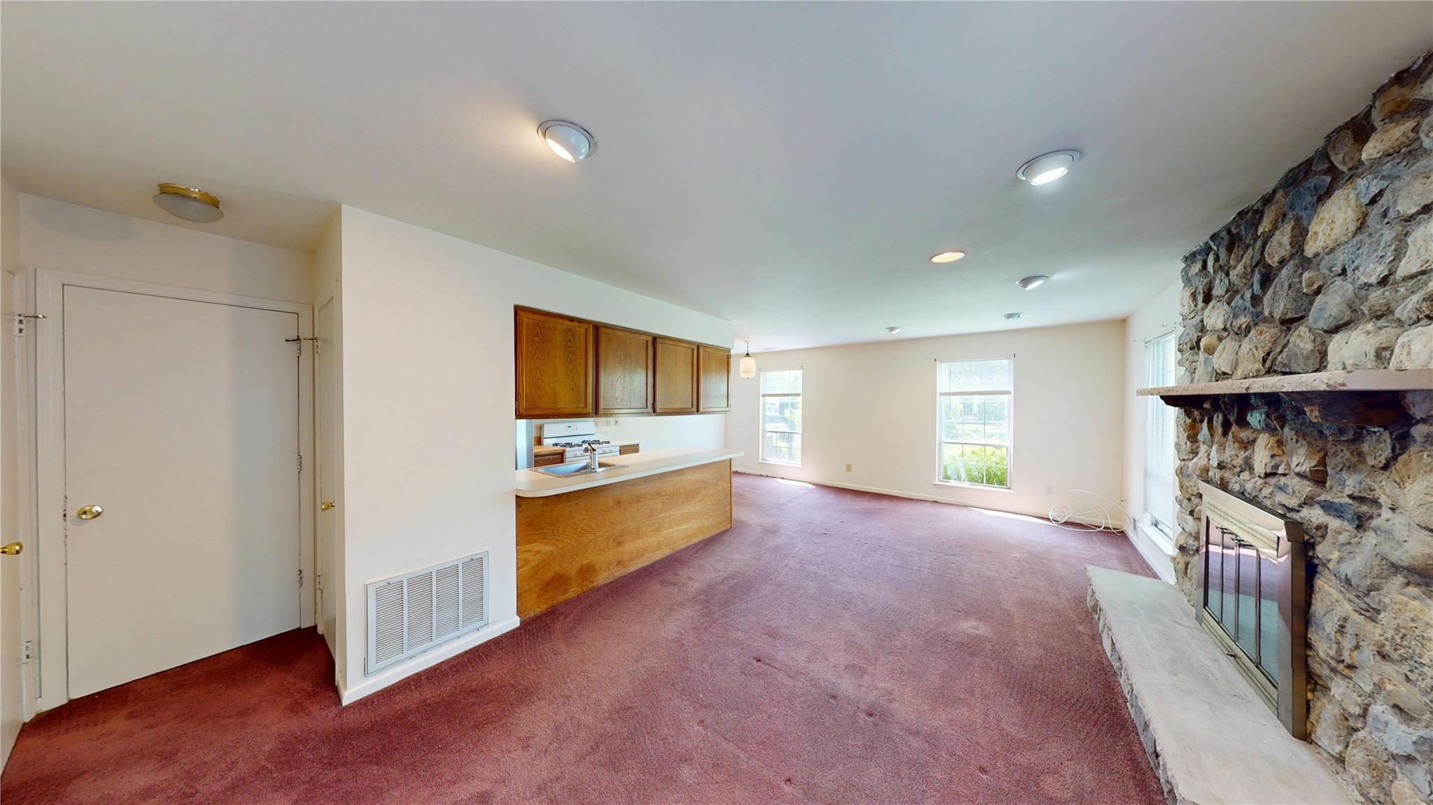 Kitchen with brown cabinetry, carpet floors, a stone fireplace, and light countertops