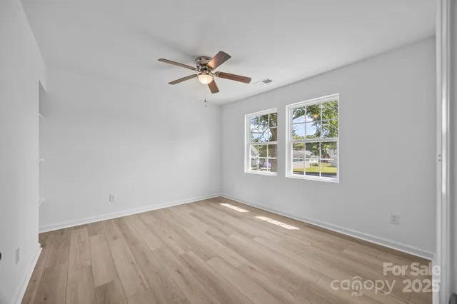 a view of empty room with wooden floor and fan