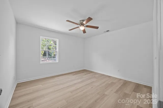 an empty room with wooden floor ceiling fan and windows