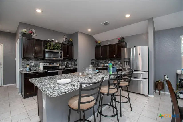 a kitchen with stainless steel appliances kitchen island granite countertop a refrigerator a stove a microwave oven a sink with island and chairs in it