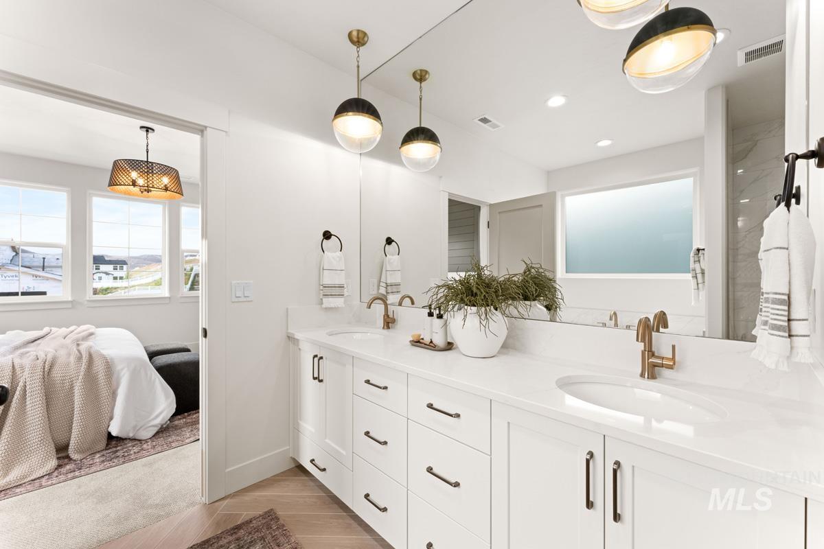 13338 North Spring Creek Way Boise, ID 83714 - Photo 22 of 46 Double vanity with white cabinetry, integrated sinks, brass-finish fixtures, and a full-width mirror