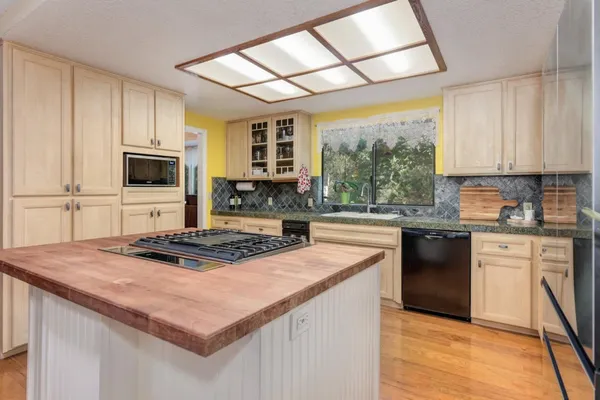 a kitchen with stainless steel appliances granite countertop a stove a sink dishwasher and white cabinets next to a window