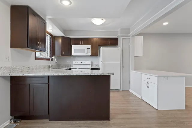 a kitchen with granite countertop a refrigerator a stove a sink and white cabinets with wooden floor