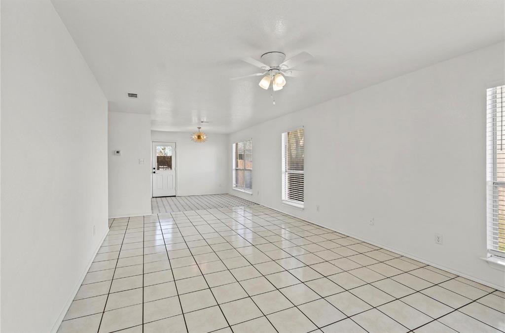 5169 East Rim Road Dallas, TX 75211 - Photo 3 of 19 Spacious interior room featuring light-toned square tile flooring with contrasting grout, multiple windows with horizontal blinds, and a ceiling fan with integrated lighting
