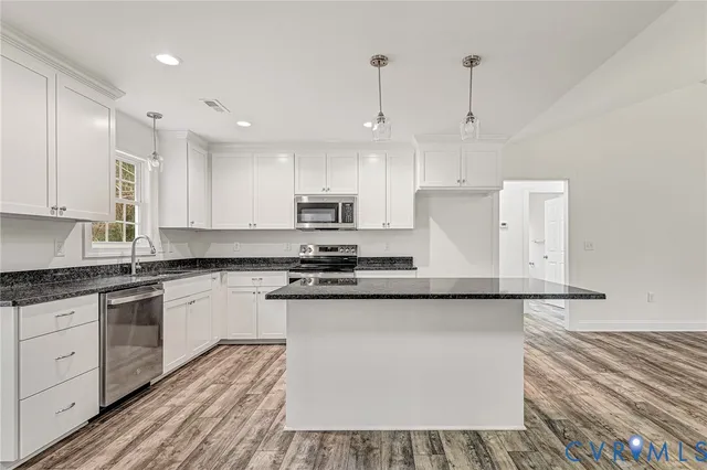 a kitchen with stainless steel appliances granite countertop a sink a stove a refrigerator and white cabinets with wooden floor