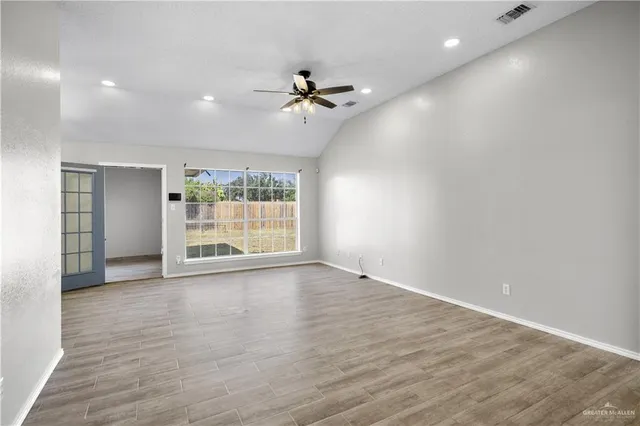 an empty room with wooden floor fan and windows