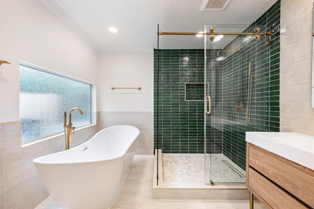 6403 Genstar Lane Dallas, TX 75252 - Photo 20 of 34 Freestanding soaking tub with a floor-mounted gold-tone faucet, complemented by a walk-in shower featuring emerald green subway tile and a gold-tone sliding glass door