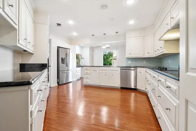 a kitchen with stainless steel appliances kitchen island granite countertop a stove a sink and white cabinets with wooden floor