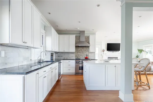 a kitchen with stainless steel appliances granite countertop a stove top oven a sink a refrigerator white cabinets and wooden floor