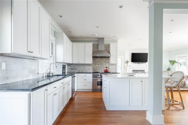 a kitchen with stainless steel appliances granite countertop a stove top oven a sink a refrigerator white cabinets and wooden floor