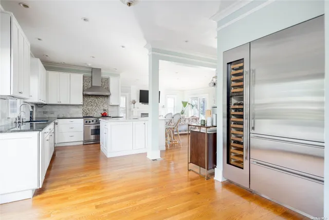 a kitchen with stainless steel appliances kitchen island granite countertop a refrigerator a stove and white cabinets with wooden floor