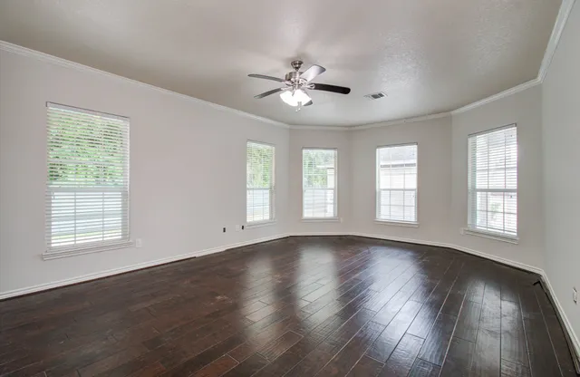 an empty room with wooden floor chandelier fan and windows