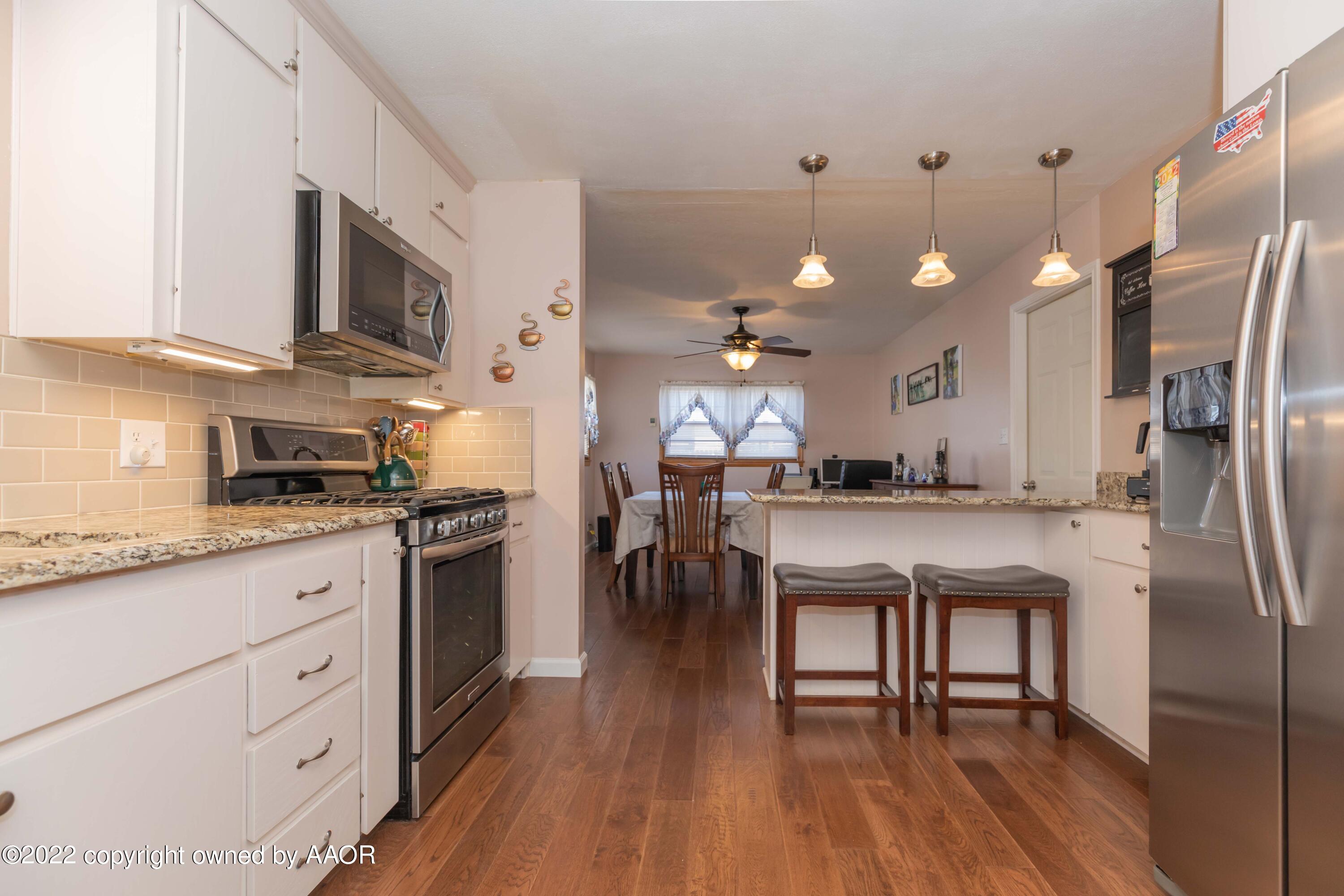 4706 South Bryan Street Amarillo, TX 79110 - Photo 8 of 40 a kitchen with stainless steel appliances granite countertop a refrigerator a sink dishwasher a stove and white cabinets with wooden floor