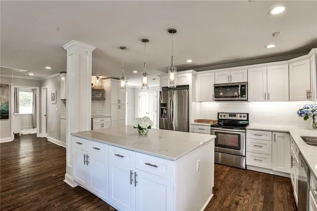 a kitchen with stainless steel appliances kitchen island granite countertop a stove a sink a refrigerator and a white cabinets with wooden floor