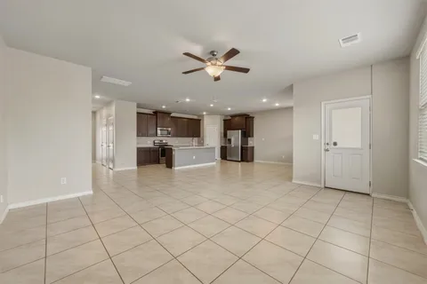 a view of an empty room and kitchen space with a ceiling fan