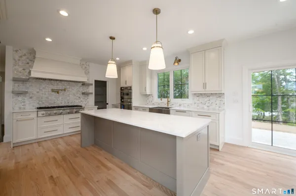 a large white kitchen with a large island oven a stove and a wooden floors