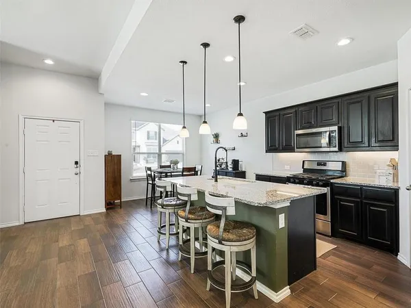 a kitchen with stainless steel appliances a stove a sink a microwave a center island and a wooden floor