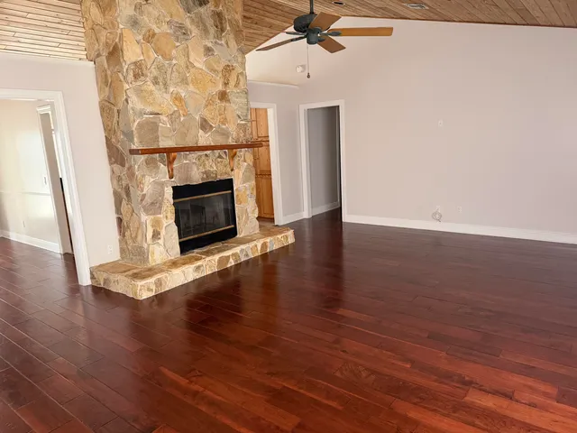 an empty room with wooden floor fireplace and windows