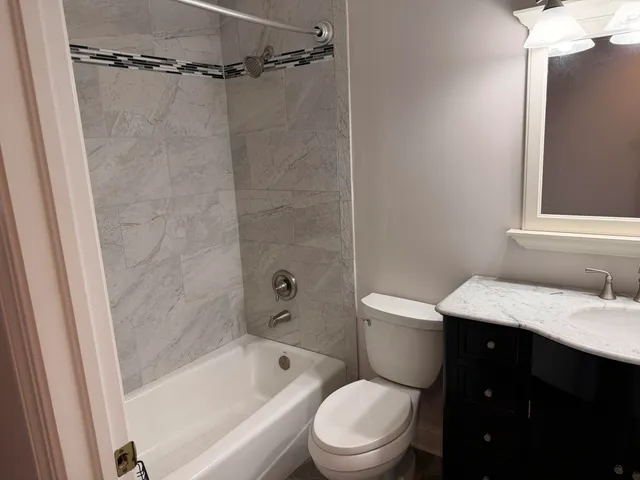 a bathroom with a granite countertop bathtub shower sink vanity and toilet