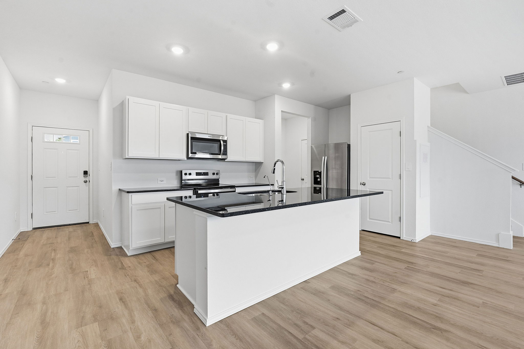 164 Cinnabar Lane, Unit 4 Kyle, TX 78640 - Photo 7 of 23 Modern kitchen featuring white cabinetry, dark countertops, a central island with a sink, stainless steel appliances, and wood-finish flooring