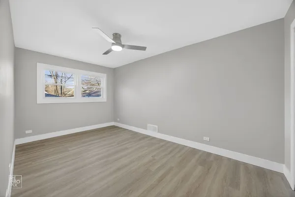 an empty room with wooden floor ceiling fan and windows