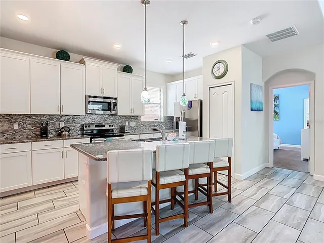 a kitchen with stainless steel appliances kitchen island granite countertop a table chairs sink and cabinets