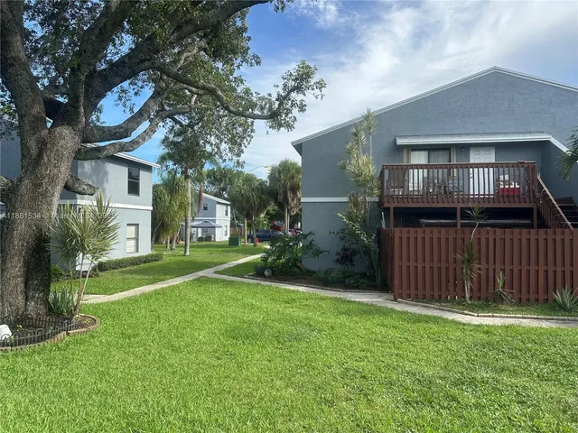 a view of a brick house with a big yard plants and large trees