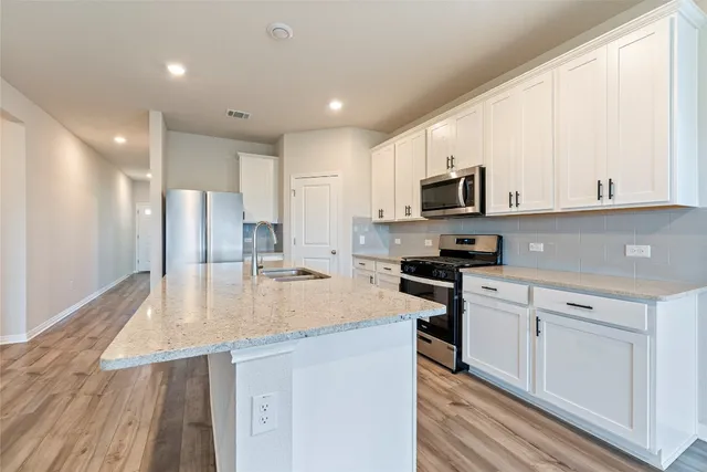 a kitchen with stainless steel appliances granite countertop a refrigerator a stove top oven a sink and dishwasher with wooden floor