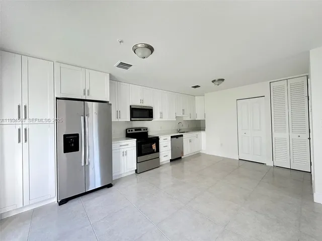 a large white kitchen with refrigerator a stove a sink and white cabinets