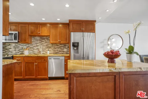a kitchen with stainless steel appliances granite countertop a sink a refrigerator and a wooden cabinets