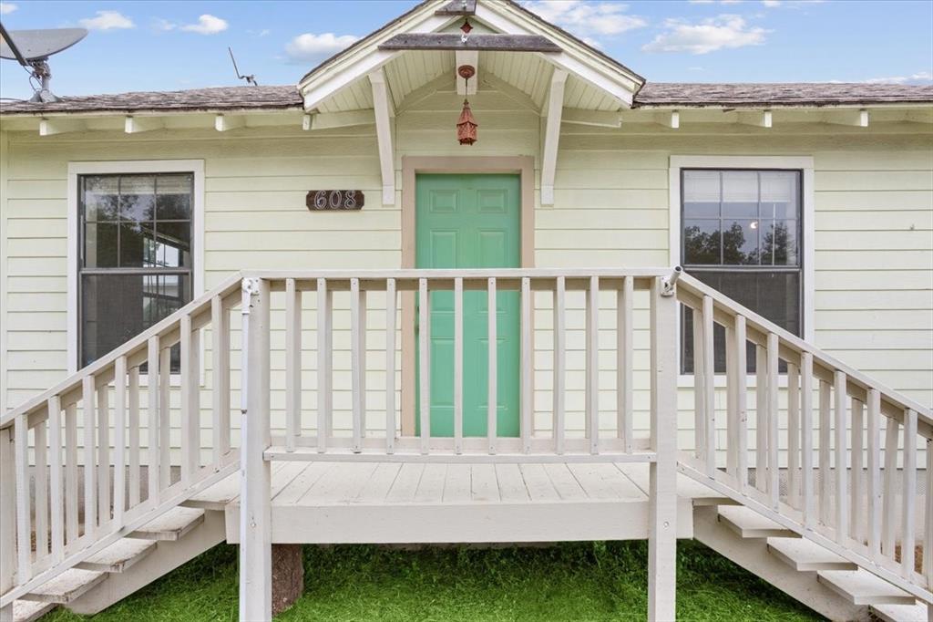 608 9th Street Hico, TX 76457 - Photo 3 of 23 Front exterior with a porch featuring wooden railing, a vibrant green entry door, light-colored horizontal siding, and two single-hung windows with white trim