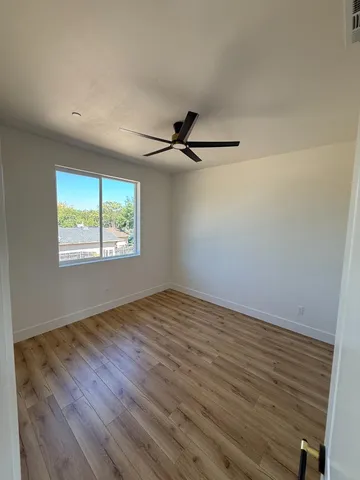 an empty room with wooden floor fan and windows