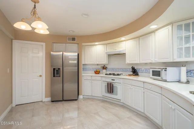 a kitchen with stainless steel appliances granite countertop a refrigerator a sink dishwasher a stove and white cabinets with wooden floor