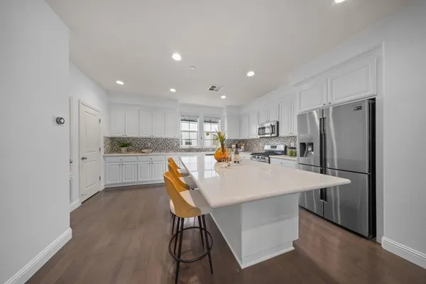 a kitchen with stainless steel appliances granite countertop a refrigerator a sink dishwasher a stove with white cabinets and wooden floor