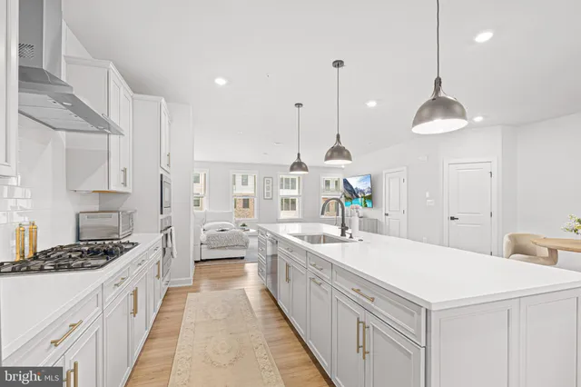 a large white kitchen with a stove a sink a center island and a wooden floor