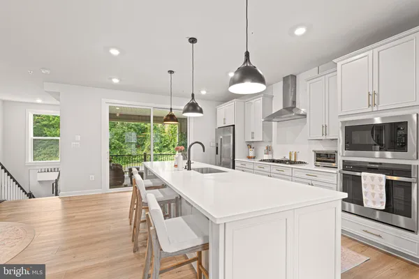 a kitchen with stainless steel appliances kitchen island granite countertop a stove a sink a microwave a refrigerator and white cabinets with wooden floor