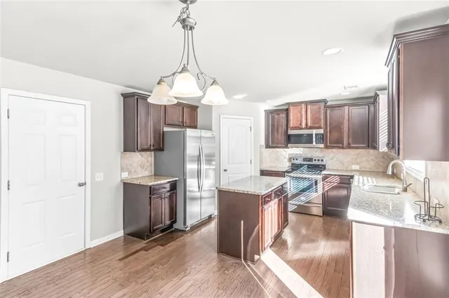 a kitchen with stainless steel appliances granite countertop a refrigerator a sink dishwasher a stove and a dining table with wooden floor