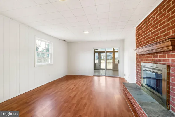 a view of an empty room with wooden floor fireplace and a window