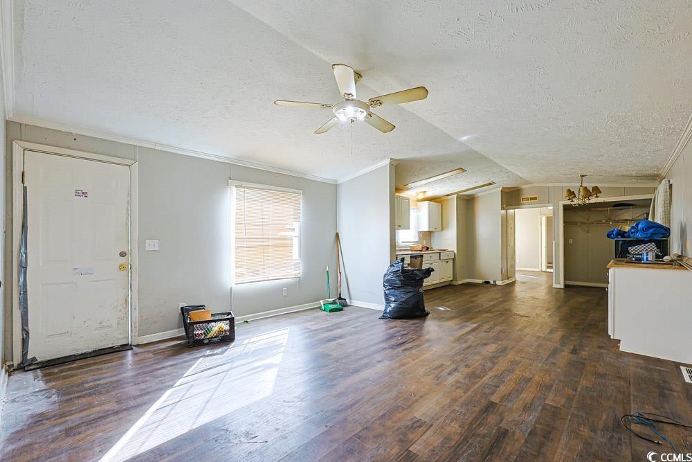 175 Darlene Drive Myrtle Beach, SC 29588 - Photo 3 of 31 Unfurnished living room with a textured ceiling, crown molding, lofted ceiling, dark wood-style flooring, and a ceiling fan