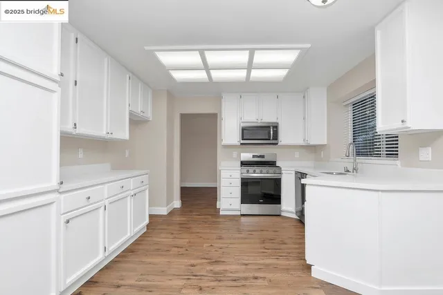 a kitchen with stainless steel appliances a stove top oven a sink a refrigerator white cabinets and wooden floor