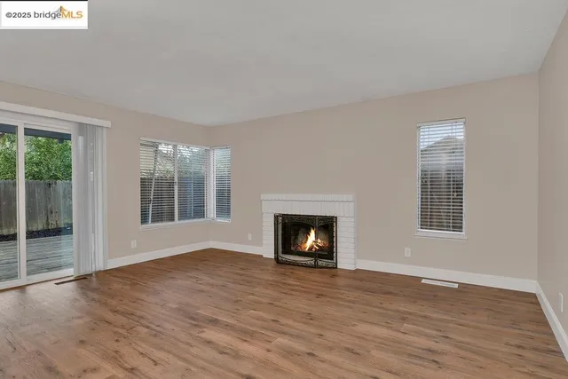 a view of an empty room with wooden floor fireplace and a window