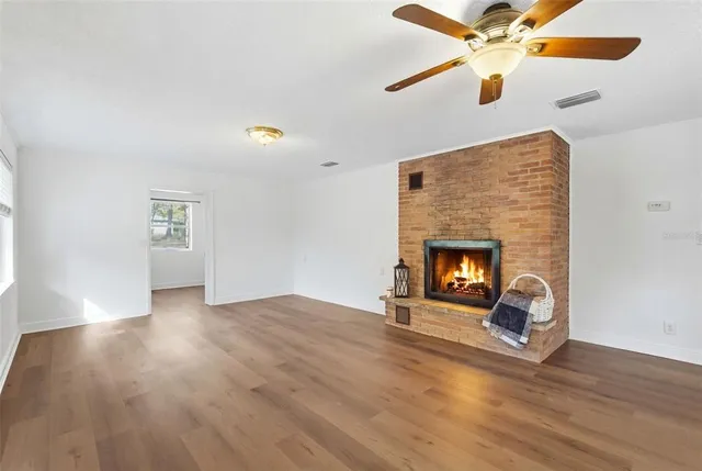 a view of an empty room with wooden floor fireplace and a window