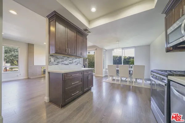 a kitchen with stainless steel appliances granite countertop a stove top oven a sink dishwasher and a dining table with wooden floor