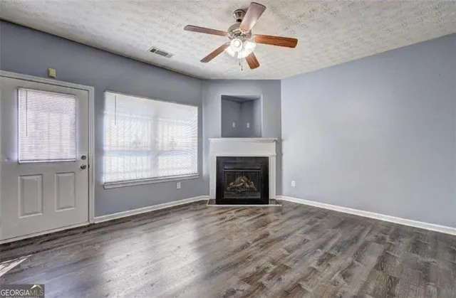 a view of a livingroom with a fireplace a ceiling fan and windows