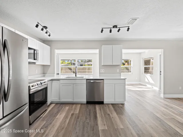 a kitchen with granite countertop a refrigerator oven a sink dishwasher and white cabinets with wooden floor